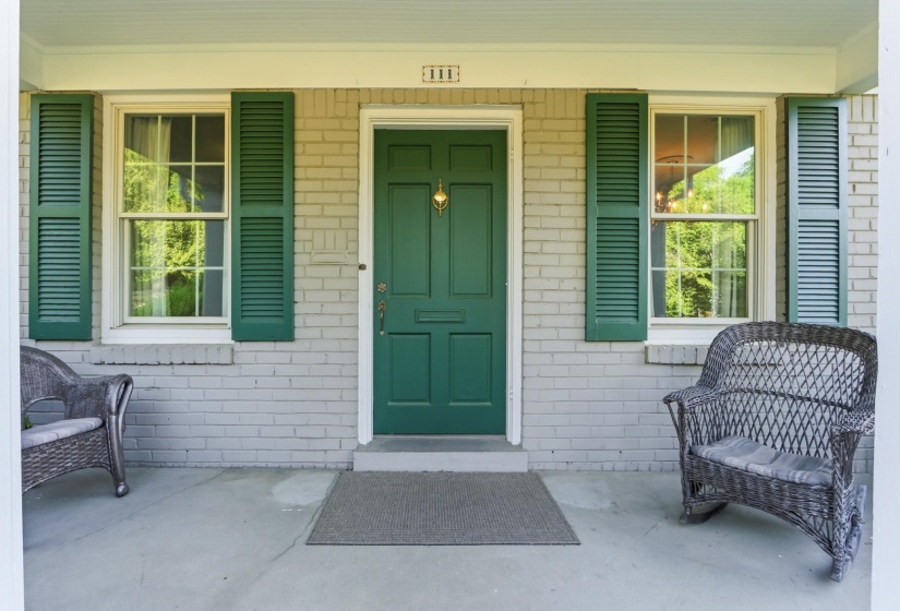 Front entrance featuring a paneled green door with a brass knocker, flanked by double-hung windows with green louvered shutters