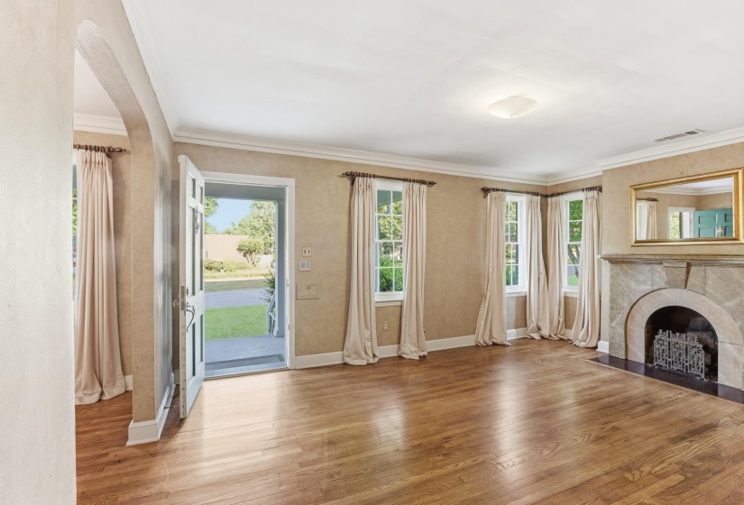 Hardwood flooring throughout a living area featuring a stone fireplace with iron grate, multiple windows, and crown molding