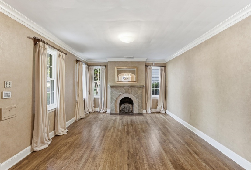Living room featuring a stone fireplace with hearth, wood-finish flooring, multiple double-hung windows, and crown molding