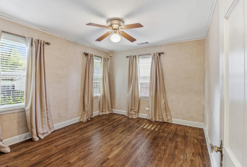 Spacious room featuring wood-finish flooring, a ceiling fan with integrated lighting, two windows with blinds, and crown molding