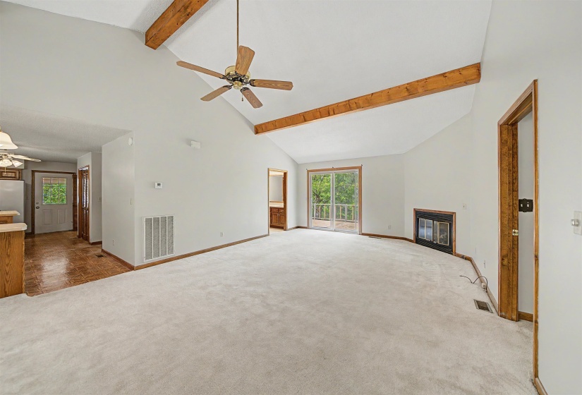 Spacious living area featuring a vaulted ceiling with exposed wood beams, a ceiling fan, and light-toned carpet flooring