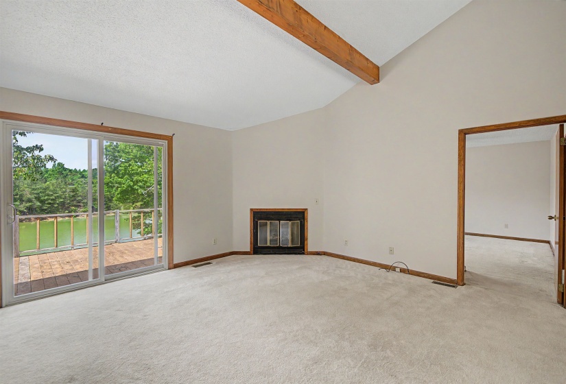 Living area featuring vaulted ceilings with exposed wood beams, a fireplace, and wall-to-wall carpeting