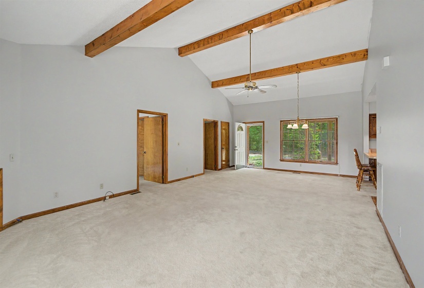 Spacious living area featuring a vaulted ceiling with exposed wood beams, neutral carpeting, and light gray walls