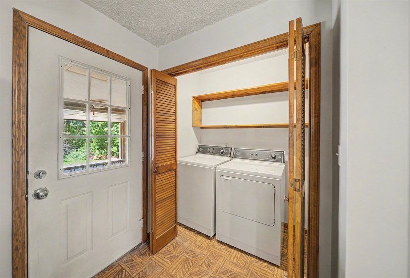 Dedicated laundry area featuring a washer and dryer, wood-finish shelving, and bi-fold louvered doors