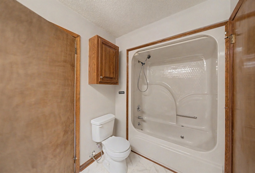 Bathroom featuring a white bathtub and shower combination with a textured back panel, chrome fixtures, and a grab bar