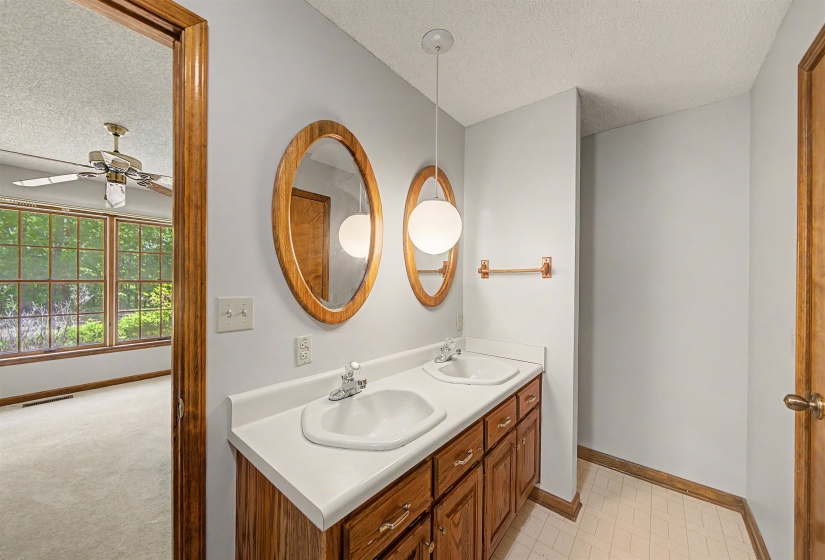Bathroom featuring a double vanity with white countertops, oval mirrors with wood frames, and wood-finish cabinetry