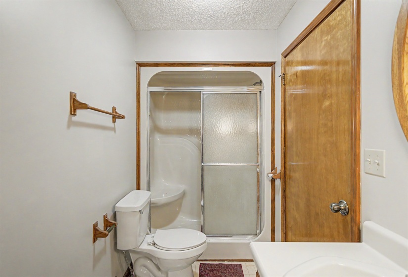 Bathroom featuring a white toilet, enclosed shower with frosted glass, wood-finish trim, and a built-in vanity with a basin sink