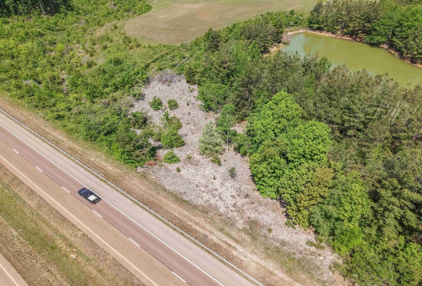 Expansive land parcel featuring a visible roadway, dense tree coverage, and a natural pond