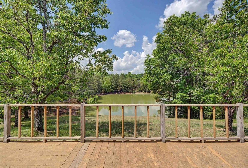 Wood-plank outdoor deck with natural wood railing, surrounded by mature trees, and overlooking a tranquil body of water