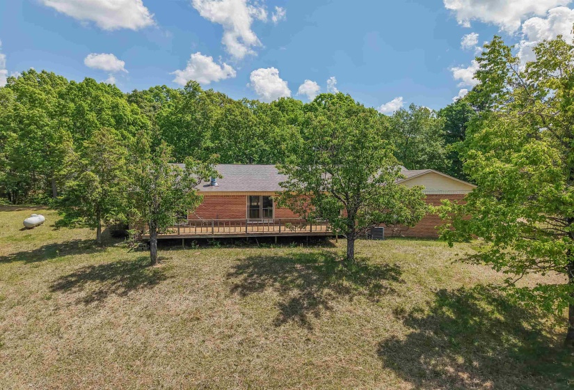 Brick exterior home with a back deck, surrounded by mature trees and natural landscaping