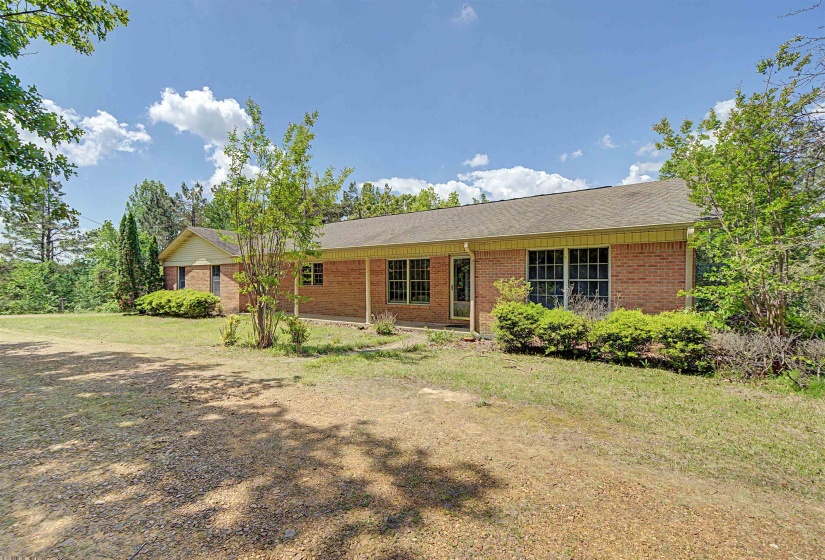 Brick exterior featuring a covered front porch, multiple windows, and surrounding mature trees