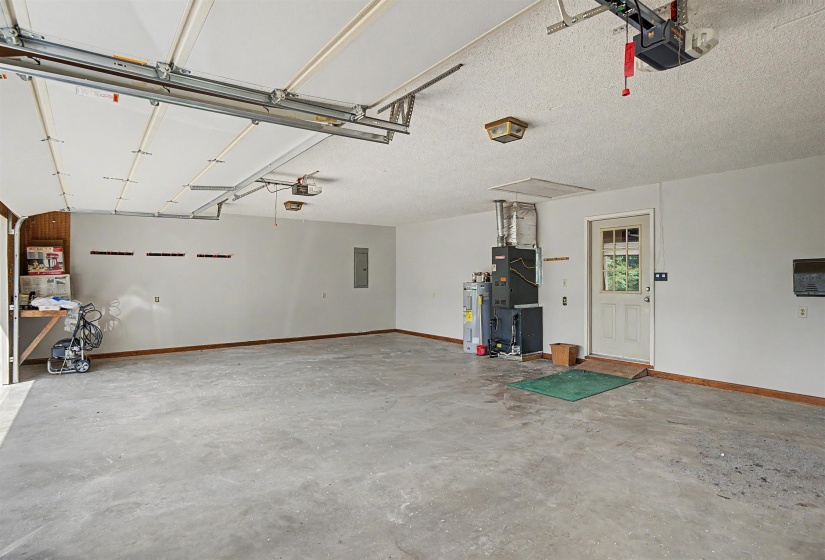 Spacious garage featuring a concrete floor, white walls, exposed ceiling joists, an interior access door, and a built-in workbench