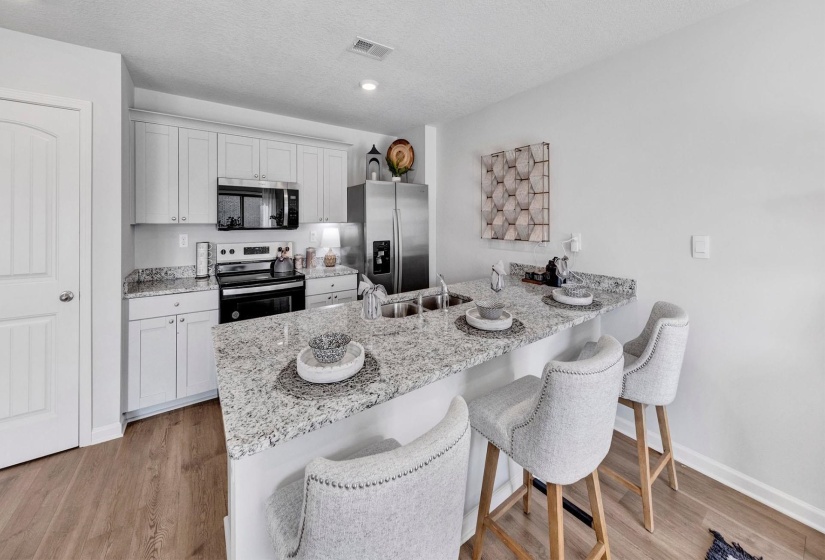 Kitchen featuring a breakfast bar area, a peninsula, appliances with stainless steel finishes, light stone counters, and light wood-style floors
