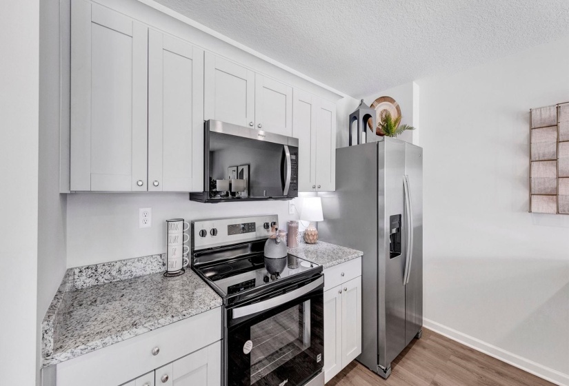 Kitchen featuring stainless steel appliances, white cabinetry, a textured ceiling, light wood-type flooring, and light stone counters