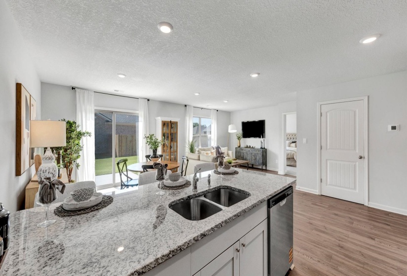 Kitchen with a textured ceiling, dishwasher, light stone counters, open floor plan, and light wood-type flooring