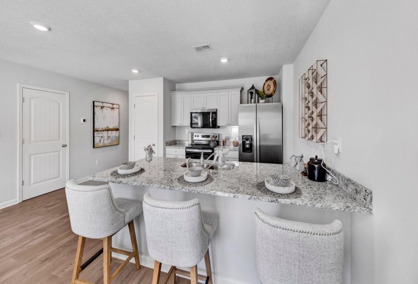 Kitchen with a breakfast bar, stainless steel appliances, a peninsula, light stone countertops, and light wood-style floors
