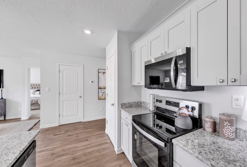 Kitchen with appliances with stainless steel finishes, light stone counters, a textured ceiling, light wood finished floors, and white cabinetry