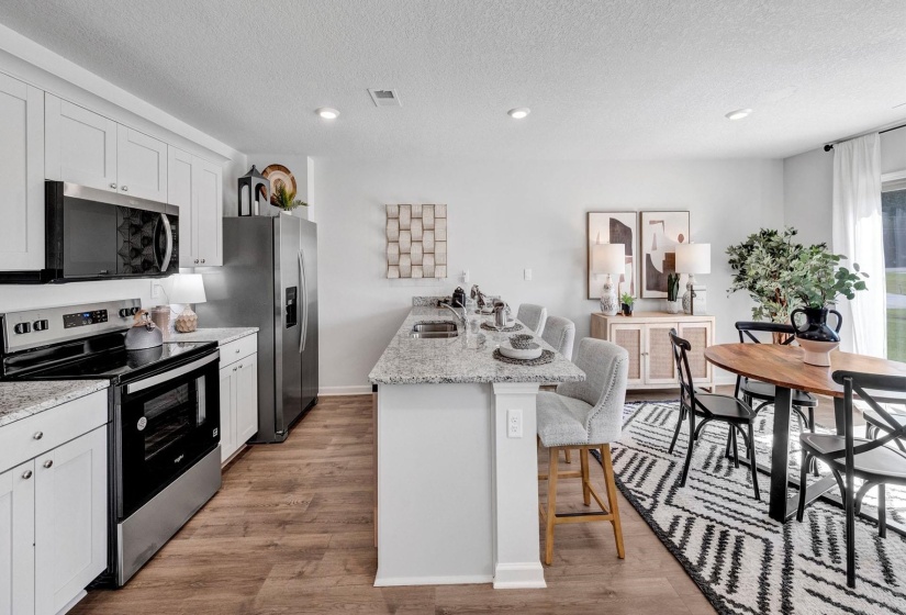 Kitchen featuring stainless steel appliances, a breakfast bar, a peninsula, light stone countertops, and light wood-type flooring