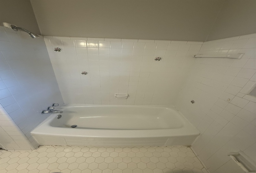 White bathtub and shower surround with decorative floral accent tiles