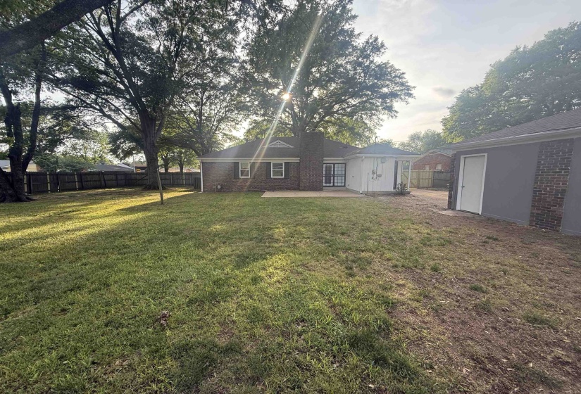 Spacious backyard featuring a brick exterior home, mature trees, a privacy fence, and an attached storage structure