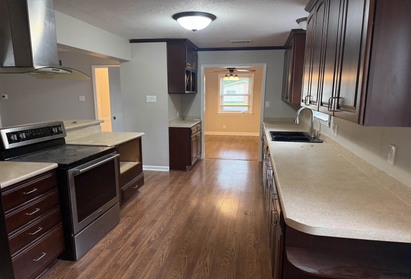 Kitchen featuring wood-finish flooring, dark wood cabinetry, light-toned countertops, and stainless steel appliances including a range with an overhead vent hood