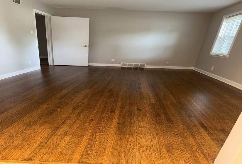 Hardwood flooring throughout this room, featuring a neutral wall color, white baseboards, and a window with blinds