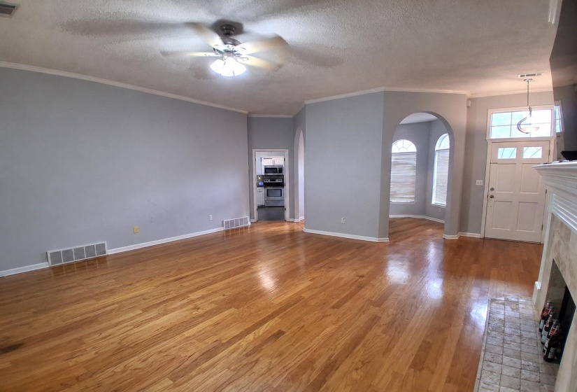Spacious living area featuring polished wood-finish flooring, crown molding, and a ceiling fan with integrated lighting