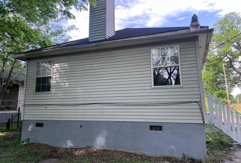 Light-colored siding exterior featuring two windows, a painted foundation, and a chimney