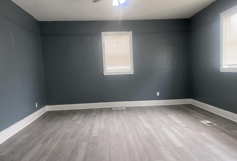 Spacious room featuring wood-finish flooring, dark accent walls, white trim, and multiple windows with blinds