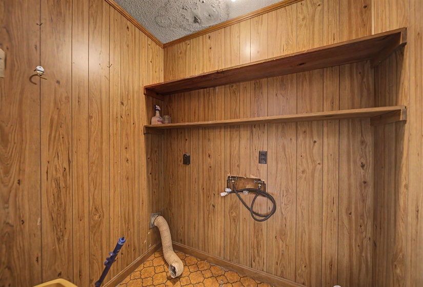 Utility area featuring wood paneling, open wood shelving, and patterned linoleum flooring