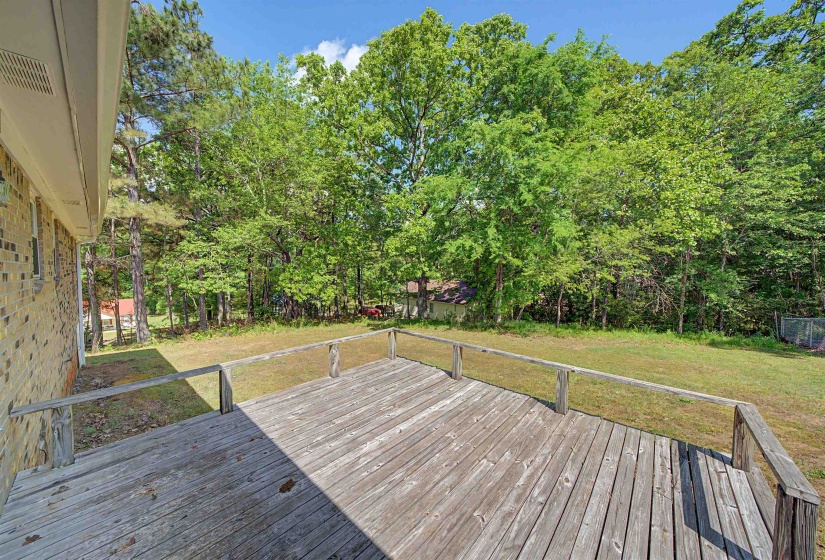 Spacious wood deck extending to a grassy area, bordered by extensive mature trees