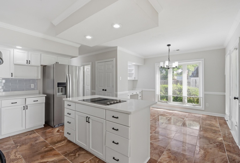 Spacious kitchen featuring an island cooktop, stainless steel appliances, white cabinetry with dark hardware, a tiled backsplash, and glossy tile flooring