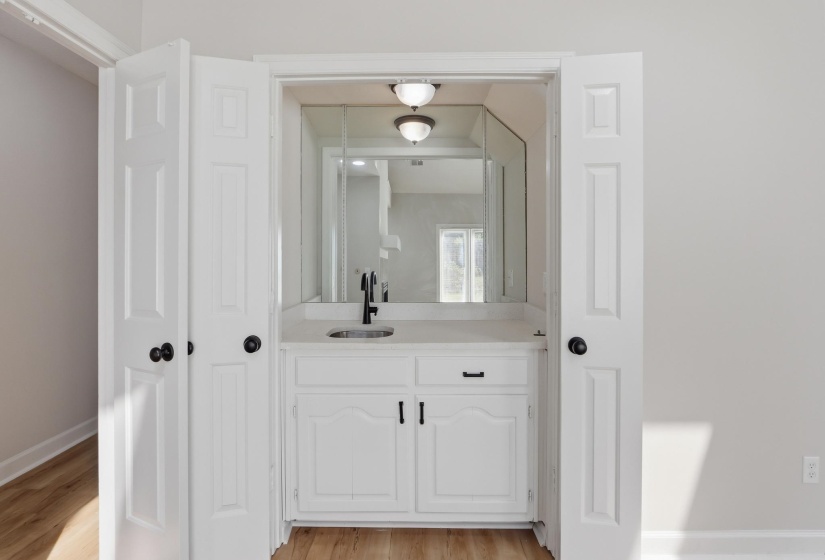 Built-in wet bar featuring a white cabinet with black hardware, a light-toned countertop, and a single basin sink with a matte black faucet