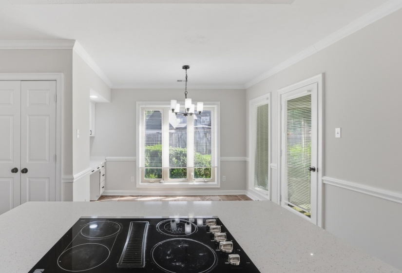 Kitchen counter with built-in cooktop, quartz-finish surface, crown molding, chair rail molding, and a chandelier-style light fixture