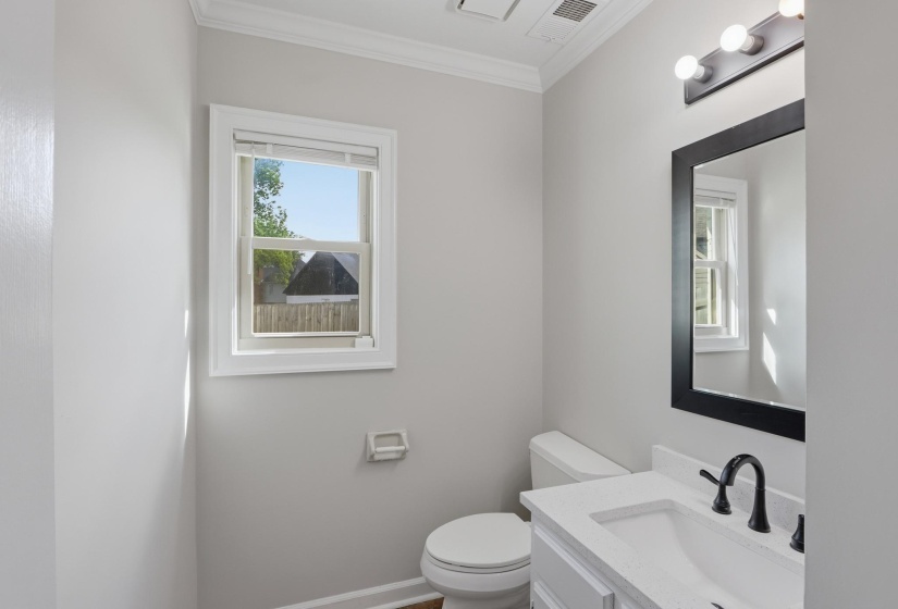 Bathroom featuring a vanity with a white countertop and integrated sink, a dark-framed mirror, and a window with white trim