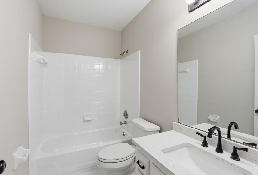 Bathroom featuring a white tub/shower combination with subway tile surround, white toilet, and a vanity with a white quartz-finish countertop, undermount sink, and matte black fixtures