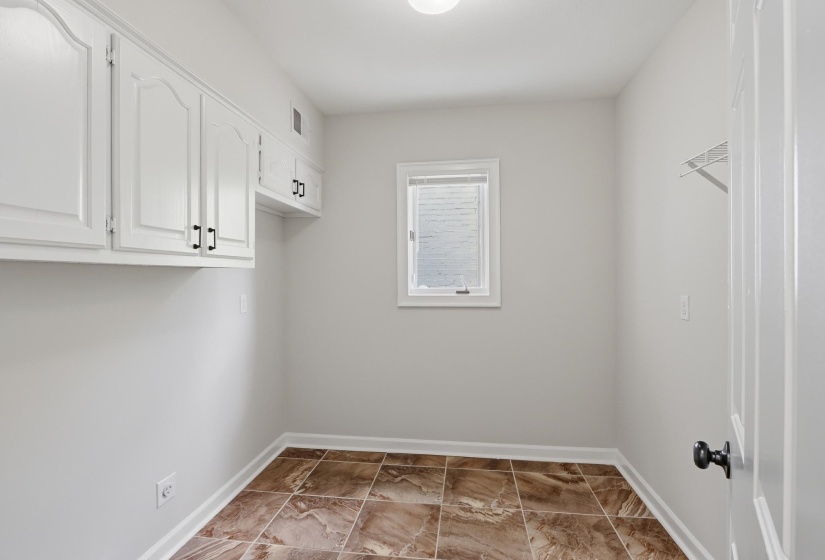 Utility room featuring white cabinetry with black hardware, a single window, and tiled flooring