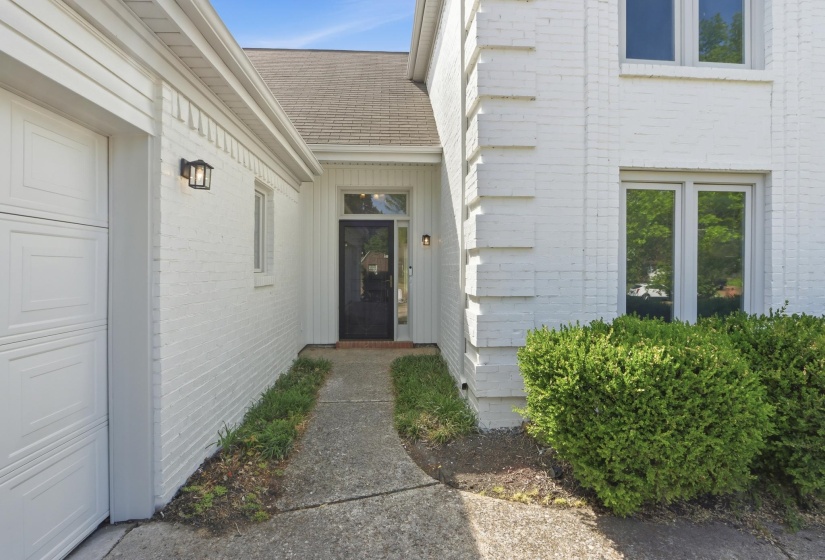 White-painted brick exterior featuring a black entry door with sidelights, a textured garage door, and a concrete walkway