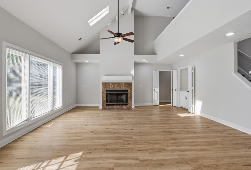 Spacious living area featuring a vaulted ceiling with skylights, a ceiling fan, and wood-finish flooring