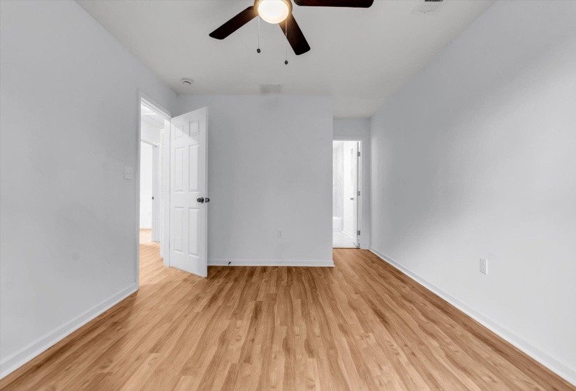 Spacious room featuring wood-finish flooring, white walls, and a ceiling fan with integrated lighting