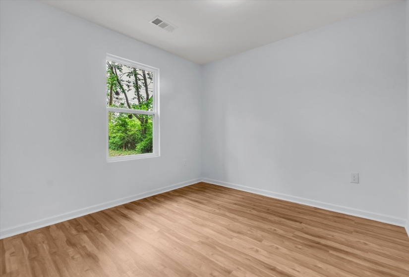Bright interior space with wood-finish flooring, white walls, and a single window offering a verdant outdoor scene