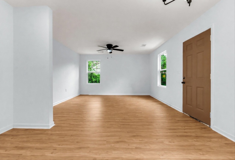 Open-concept room featuring wood-finish flooring, white walls, multiple windows, a ceiling fan, and a paneled entry door