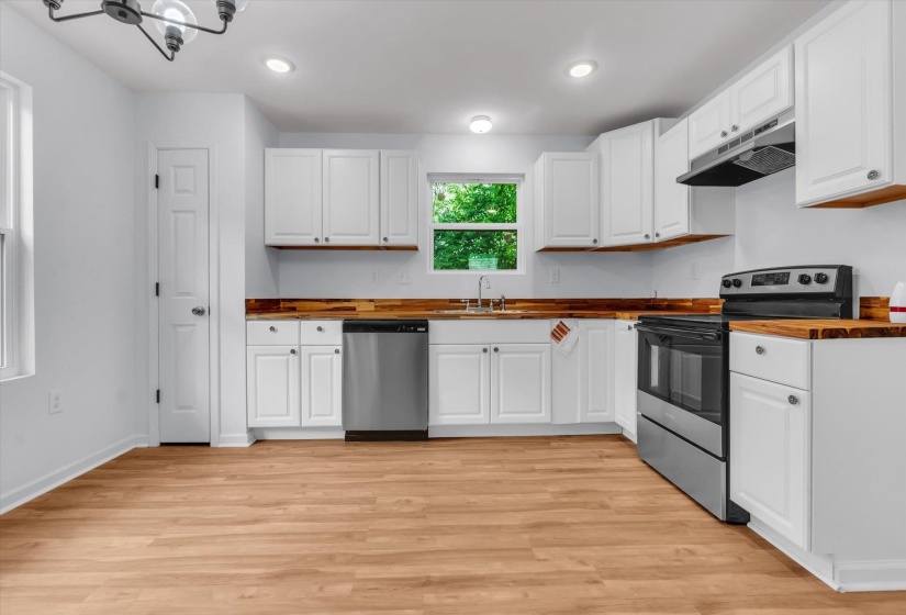 Kitchen featuring wood-finish flooring, white cabinetry with silver hardware, wood-finish countertops, stainless steel appliances, and recessed lighting