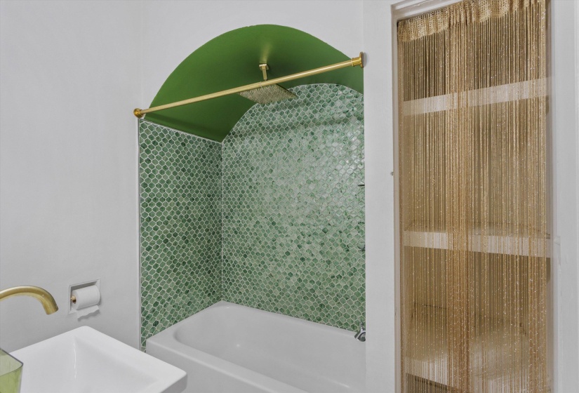 Arched bathtub enclosure featuring green scallop-patterned tile and a gold rain showerhead