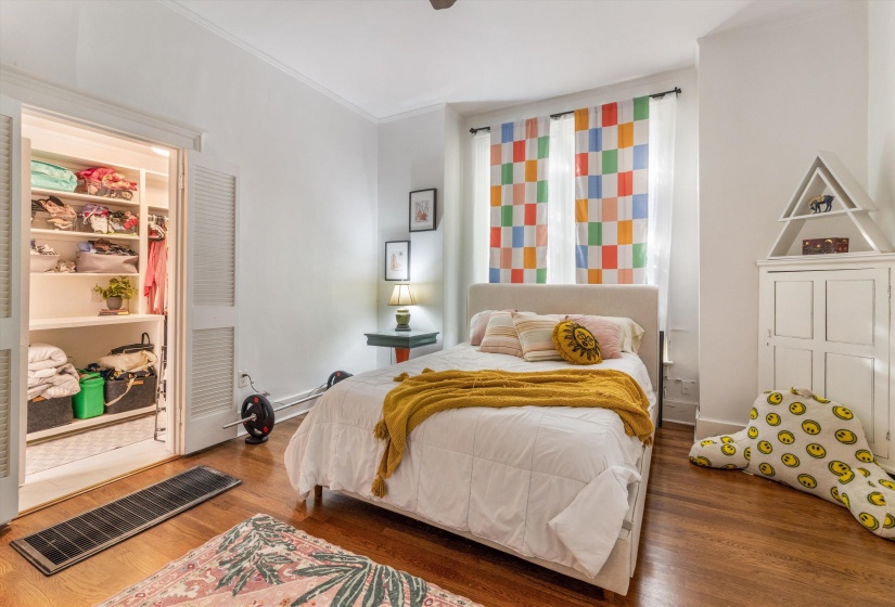 Bright bedroom featuring hardwood flooring, white walls, a built-in closet with louvered bifold doors, and a window with natural light