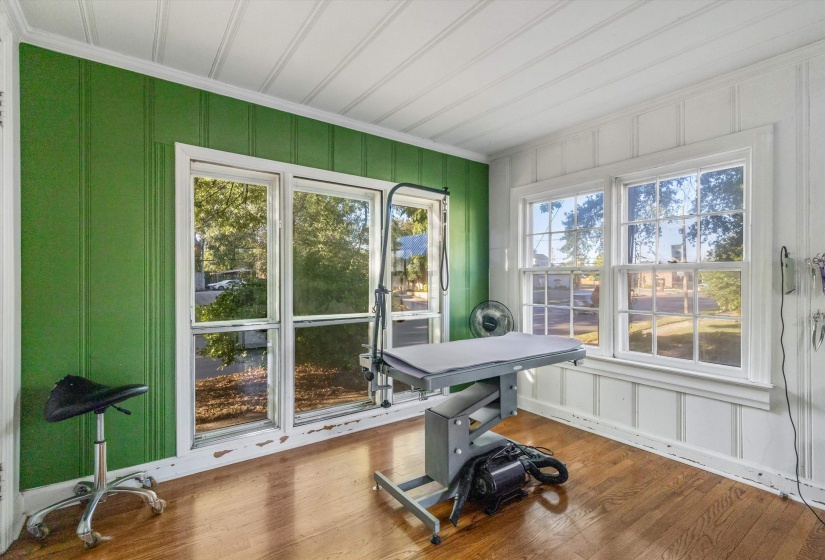 Room featuring wood-finish flooring, white paneled walls, a green accent wall with vertical paneling, and multiple windows providing natural light