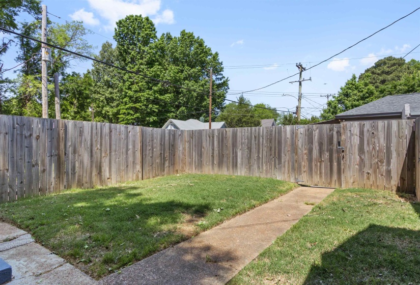 Fenced backyard featuring a grassy area, a concrete pathway, and a wooden privacy fence