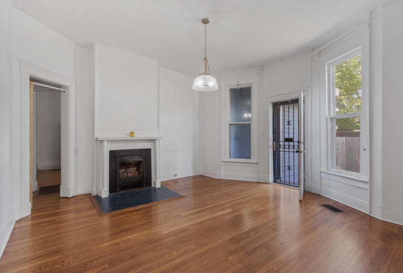 Hardwood flooring throughout a room featuring a white mantel fireplace with a dark tile hearth