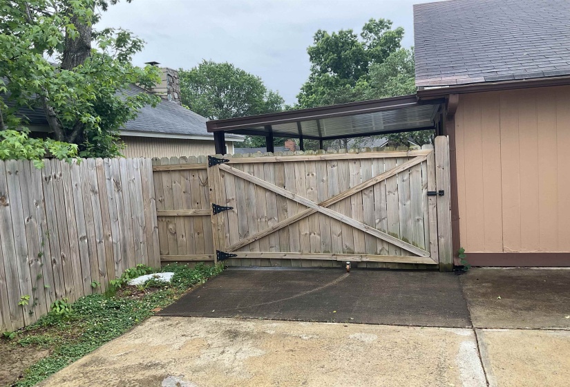 Wood privacy fence with an X-brace gate, concrete pad, and covered walkway