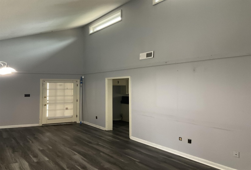 Vaulted ceiling with transom windows, wood-finish flooring, white baseboards, and a glass-paneled door
